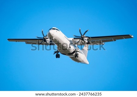 An ATR 72 airplane, a twin-engine turboprop short-haul regional passenger aircraft. Landing airplane. Blue background. Royalty-Free Stock Photo #2437766235