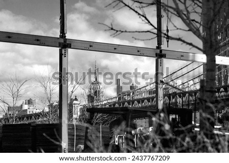 black and white new york city - the Empire State Building seen through scaffolding in Brooklyn with the end of the Manhattan Bridge just visible Royalty-Free Stock Photo #2437767209