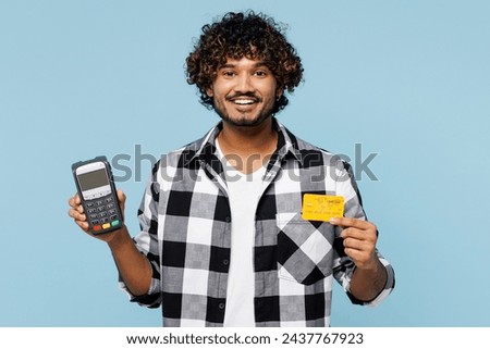 Young Indian man he wears shirt white t-shirt casual clothes hold wireless modern bank payment terminal to process acquire credit card isolated on plain pastel blue cyan background. Lifestyle concept