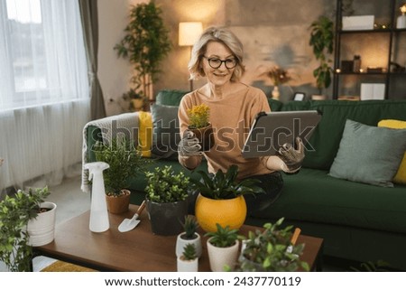 one woman florist take care grow cultivate plants at home hold digital tablet search online advice or use app application