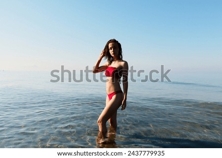 Young bikini model at the beach in red swimsuit. Summer holiday at the seaside where you can swim and play in the heat. Ready western european woman walking relaxing during a travel vacation