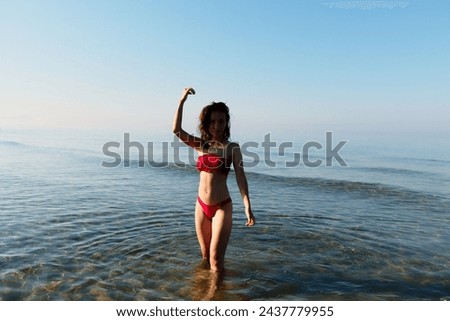Young bikini model at the beach in red swimsuit. Summer holiday at the seaside where you can swim and play in the heat. Ready western european woman walking relaxing during a travel vacation Royalty-Free Stock Photo #2437779955