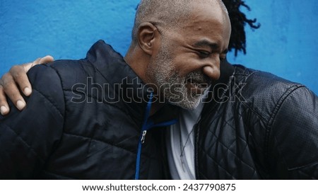 African American adult son hugging middle-aged father in genuine caring moment between parent and offspring, putting foreheads together and embcrace on blue urban backdrop Royalty-Free Stock Photo #2437790875