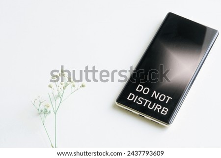 Modern smartphone - cell phone with inscription do not disturb and lonely green dried flower white background. The concept of rest and solitude. Loneliness and depression. Photo. Close-up Royalty-Free Stock Photo #2437793609