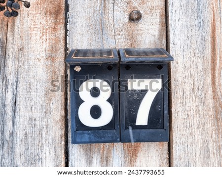 Number 87 on a Blue Sign Against Wooden Background. A bold white number 87 centered on weathered blue square sign