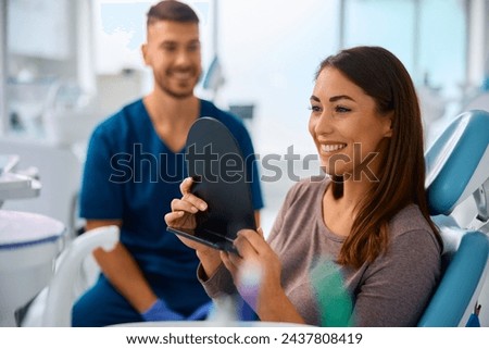 Satisfied woman looking herself in a mirror during a visit to the dentist. Royalty-Free Stock Photo #2437808419
