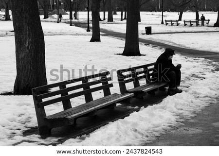 Black and white picture of a lonely person with mask sitting on a bench in Downtown Boston, during Covid-19 pandemic, at Christmas Eve of 2020