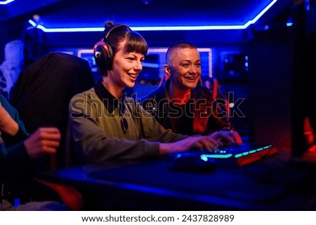 Smiling woman gamer playing PC video game and having fun with her friends. Female video game player participating on a cybersport tournament in a Esports arena or on a Gaming convention. Royalty-Free Stock Photo #2437828989