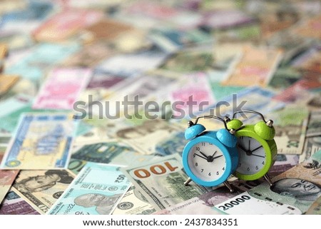 Small alarm clock on many banknotes of different currency. Background of time and money close up