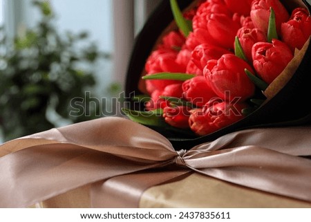 Bouquet of red tulips and a gift box with a bow, festive concept.