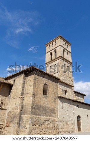 A large building with a tall tower and a blue sky in the background. The building has many arched windows and a stone facade. Sunny day at the church of Bartolome in the town of Logroño. 