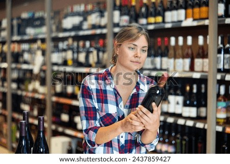 Portrait of young woman visiting winehouse in search of bottle of good wine Royalty-Free Stock Photo #2437859427