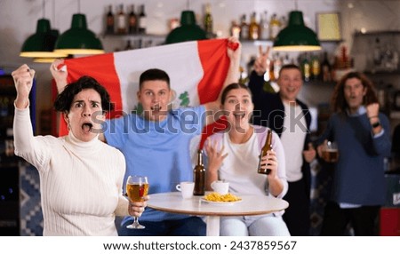 Company of emotional adult young sports fans holding flag of Peru, rejoicing winning match game and drinking beer in bar