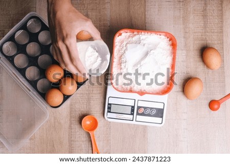 Top view of woman hand weighing flour for baking on digital scales on wooden background Royalty-Free Stock Photo #2437871223