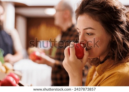 Woman smelling organic handpicked apples in zero waste supermarket while vendor talks with elderly customer in blurry background. Client testing to see if local neighborhood shop fruits are fresh Royalty-Free Stock Photo #2437873857