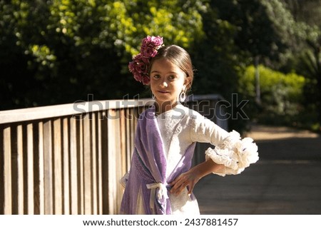 Portrait of a pretty girl dancing flamenco in a dress with frills and fringes typical of gypsies, walking on a wooden bridge in a famous park in Seville, Spain. Her hair is tied back with a flower