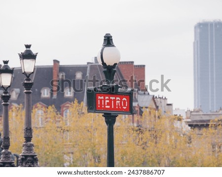 A close-up photo of a red metro sign mounted on a green metal pole. The sign is likely from the Paris Metro system, based on the design and the surrounding architecture.