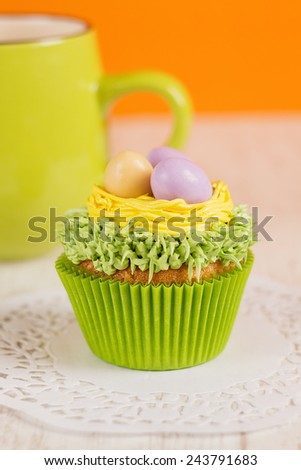 Easter cupcakes decorated with eggs in nest. Orange background with green mug. Shallow focus