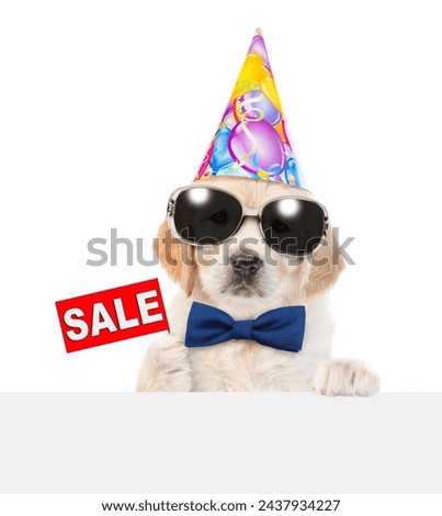 Golden retriever puppy wearing tie bow and party cap shows signboard with labeled "sale" from behind empty white banner. isolated on white background