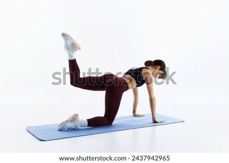 Young athletic woman in leggings and top training, standing on knees and plans and lifting leg isolated over white background. Concept of sport, health and body care, fitness app, exercises templates