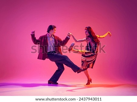 Stylish, beautiful young couple, man and woman in retro clothes dancing swing against pink background in neon light. Concept of hobby, dance class, party, 50s, 60s culture, youth Royalty-Free Stock Photo #2437943011