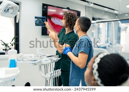 Male dentist in a dental office talking with a female colleague while looking at x-ray image of patient's teeth. Royalty-Free Stock Photo #2437945599