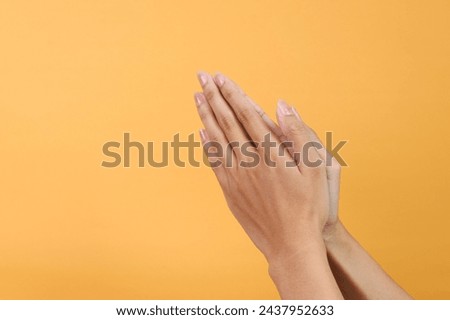 Female hands showing praying gesture against yellow background.