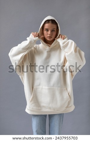 Beautiful blonde woman in a white hoodie and blue jeans posing on a gray background