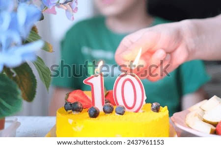 A person lighting a candle on a yellow cake with number 10
