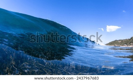 Blue clear ocean smooth glass water swimming close-up encounter wave over exposed reef with coastline beach landscape. Royalty-Free Stock Photo #2437967683