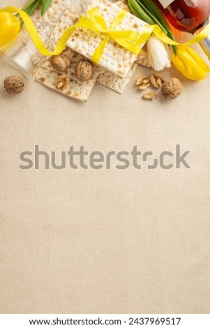 Pesach dinner display: Vertical top view picture of ribbon-wrapped matzah, wine, flute, walnuts, nestled amongst natural tulips on a beige linen table surface, with empty area for words
