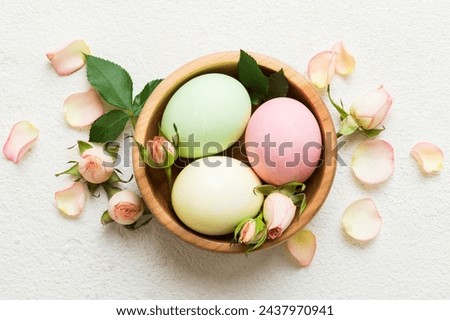 Happy Easter. Easter eggs in basket on colored table with yellow roses. Natural dyed colorful eggs background top view with copy space.