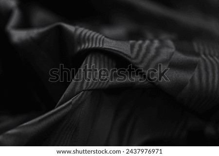 Close-up of texture of black taffeta (silk) fabric with black stripes pattern. Background, texture of draped dressy fabric with shining black stripes pattern. Royalty-Free Stock Photo #2437976971