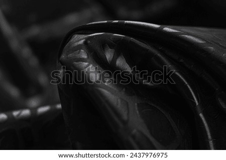 Close-up of texture of black jacquard (silk) fabric with black leopard pattern. Background, texture of draped dressy fabric with shining black abstract leopard pattern. Royalty-Free Stock Photo #2437976975
