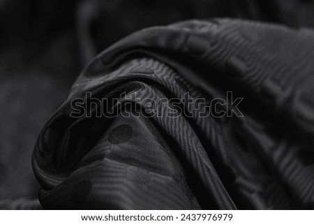 Close-up of texture of black taffeta (silk) fabric with black polka-dot pattern. Background, texture of draped dressy fabric with shining black polka-dot pattern. Royalty-Free Stock Photo #2437976979