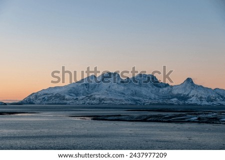 Landscape shot highlighting the rugged mountains and snow-covered beaches of arctic norway during a brief golden hour during the long winters.