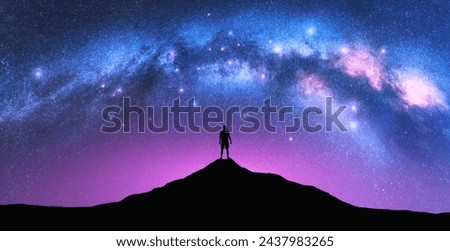 Milky Way arch and man on the mountain peak at starry night. Silhouette of alone guy, pink sky with bright stars in summer. Galaxy. Space background. Landscape with arched milky way. Travel and nature