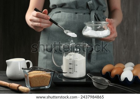 Woman adding baking powder into measuring cup at black wooden table, closeup Royalty-Free Stock Photo #2437984865
