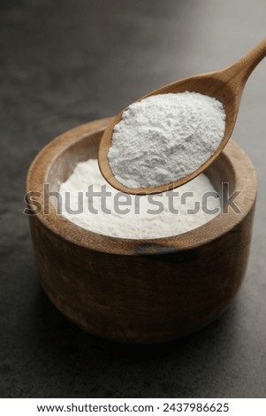 Baking powder in bowl and spoon on grey textured table, closeup