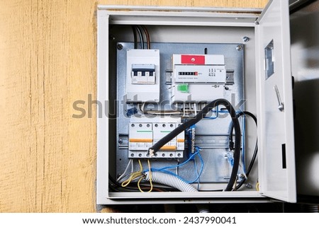 An open electrical panel is securely mounted on wooden wall, revealing an array of circuit breakers, wires, and safety switches. Royalty-Free Stock Photo #2437990041