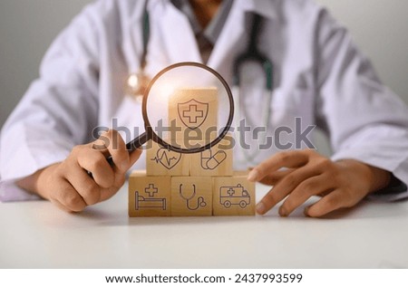 Doctor holding magnifying glass against stacked wooden cubes with medical insurance icon