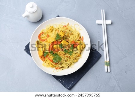 Stir-fry. Delicious cooked noodles with chicken and vegetables in bowl served on gray textured table, flat lay