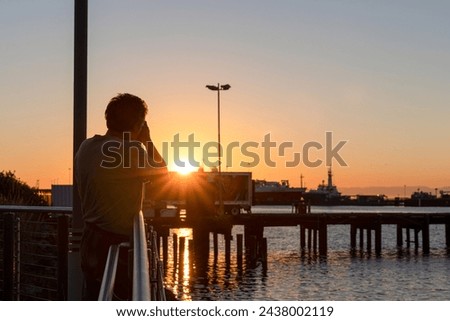 Photographer taking a picture of sunset at the Pacific Ocean and industrial ships in Port Angeles, Washington