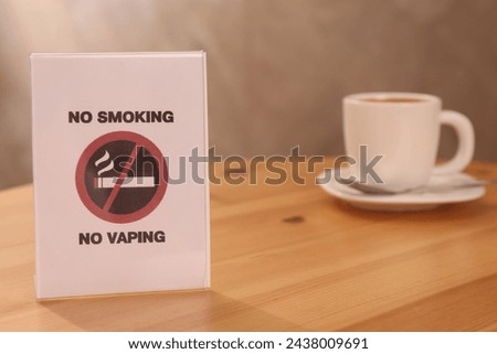 No Smoking sign and cup of drink on wooden table indoors, selective focus