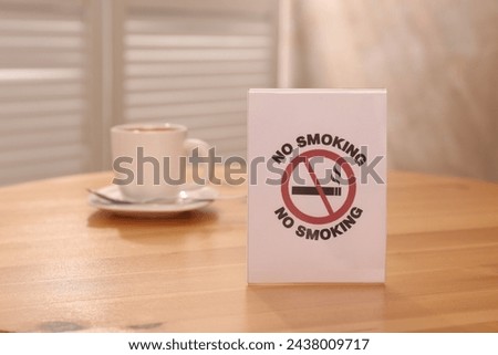 No Smoking sign and cup of drink on wooden table indoors, selective focus