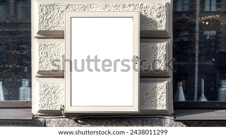 Blank white poster with mock up on building wall with beige stone facade of outdoor shop window with an electric power box at city street