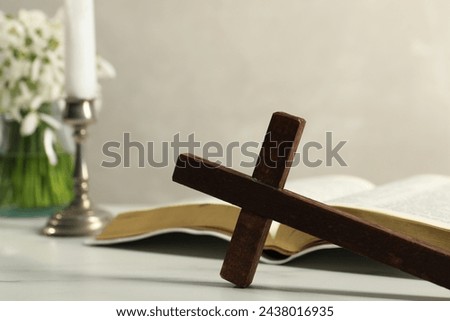 Wooden cross, Bible and church candle on white table, closeup