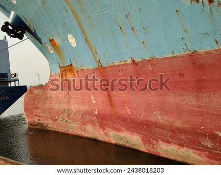 Side wall with Anchor on large cargo ship's anchor being pulled. Blue and red ship, While docked at the pier by large ropes on the river, in the background of the buildings view and transport concept