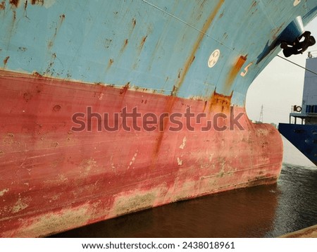 side wall with Anchor on large cargo ship's anchor being pulled. Blue and red ship, While docked at the pier by large ropes on the river, in the background is a view of the city and transport concept