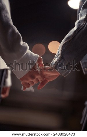 A close-up of a couple's clasped hands, set against a backdrop of soft light, evokes the closeness and warmth of their connection. Royalty-Free Stock Photo #2438028493
